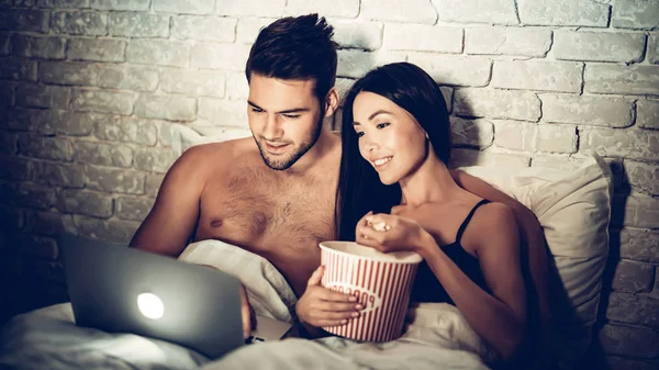 Pareja usando el ordenador portátil acostado en la cama viendo película —  Fotos de Stock