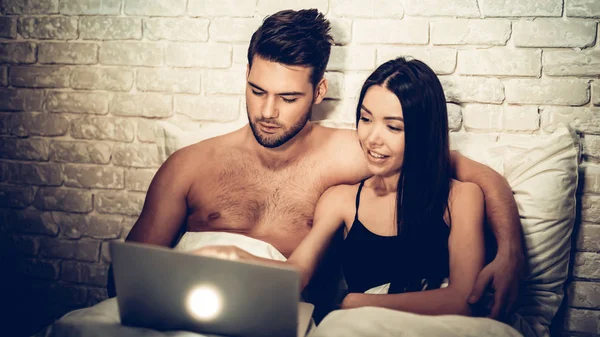 Pareja usando el ordenador portátil acostado en la cama viendo película —  Fotos de Stock