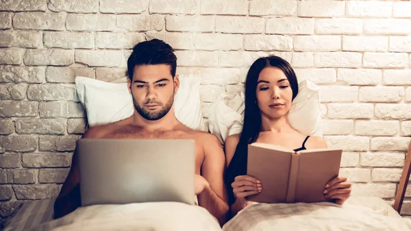 Casal usando laptop leitura livro antes de dormir — Fotografia de Stock