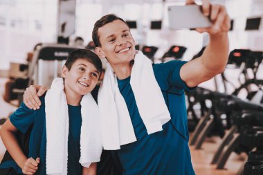 Genç baba ve oğlu Selfie Modern spor salonunda koşu bandı yakınındaki alarak. Sağlıklı yaşam konsepti. Spor ve eğitim kavramları. Smartphone kullanarak. Aile spor. Koşu izler. Anne-baba ile çocuk.