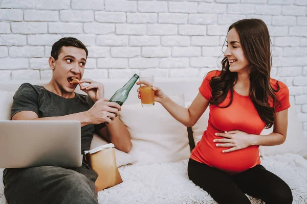 Couple Sitting Couch Pregnant Woman Drinking Juice Man Eating Chips — Stock Photo, Image