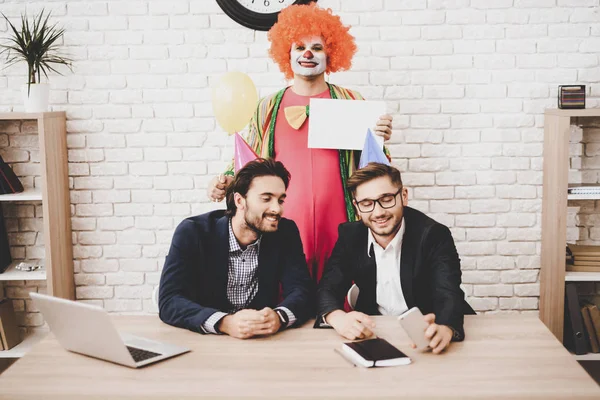Young Man in Clown Costume on Meeting in Office. April Fools Day. Businessman in Office. April Jokes. Workers on Meeting. Holidays and Celebration Concept. Clown with Baloon. Man with Red Nose.