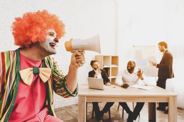 Man in Clown Costume with Loudspeaker in Office. April Fools Day. Businessman in Office. April Jokes. Crazy Day. Workers on Meeting. Holidays and Celebration Concept. Clown with Red Nose.