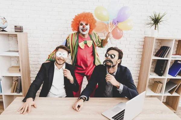 Young Man in Clown Costume on Meeting in Office. April Fools Day. Businessman in Office. April Jokes. Workers on Meeting. Holidays and Celebration Concept. Clown with Baloons. Man with Red Nose.