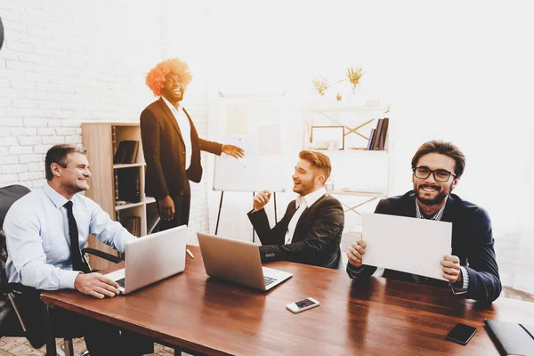 Man in Orange Wig on Business Meeting in Office. April Fools Day. Businessman in Office. April Jokes. Crazy Day. Laptop in Office. Workers on Meeting. Holidays and Celebration Concepts.