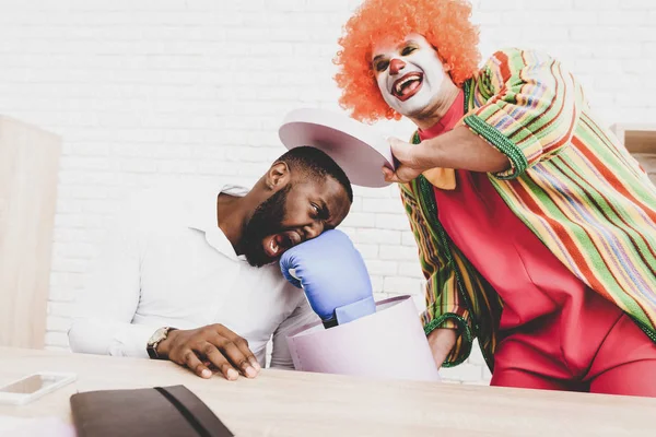 Young Man in Clown Costume on Meeting in Office. April Fools Day. Man with Gift Box. April Jokes. Crazy Day. Workers on Meeting. Holidays and Celebration Concept. Clown with Red Nose.