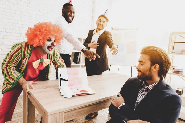 Young Man in Clown Costume on Meeting in Office. April Fools Day. Businessman in Office. April Jokes. Stickers on Laptop Workers on Meeting. Holidays and Celebration Concept. Clown with Red Nose.