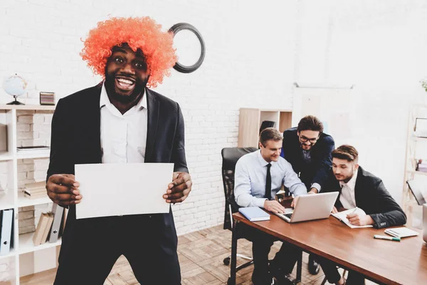 Man in Orange Wig on Business Meeting in Office. April Fools Day. Businessman in Office. April Jokes. Crazy Day. Laptop in Office. Workers on Meeting. Holidays and Celebration Concepts.