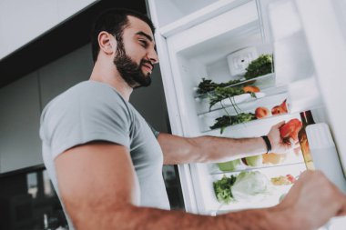 Sportif bir adam sebze buzdolabını açıp oradan alır. Mutfak konsepti. Genç ve yakışıklı. Spor vücut. Evin iç. Kapıyı aç. Sabah taze besin. Vitaminler karşılama. Sağlıklı yaşam tarzı.