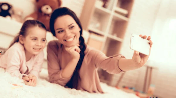 有趣的女儿 在家休息 儿童发展 微笑的妈妈和女儿 快乐的人在睡衣 女孩和妈妈躺在地毯上 彩色铅笔 微笑的妈妈和女儿 做自拍 手机在手 — 图库照片