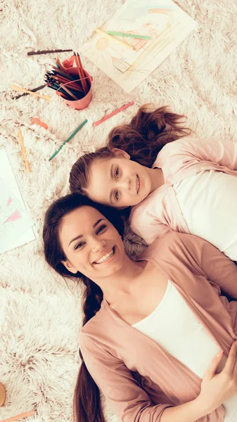 Woman Fun with Daughter. Rest at Home. Child Development. Mom and Daughter Play. Happy Mom and Child in Pajamas. Girl and Mother Lie on Carpet. Colour Pencils. Mom and Girl Lie on White Carpet.