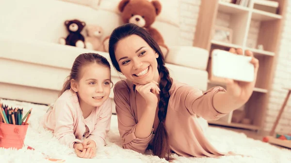 Mom Fun with Daughter. Rest at Home. Child Development. Mom and Daughter. Happy Person in Pajamas. Girl and Mother Lie on Carpet. Colour Pencils. Smiling Mom and Daughter. Make Selfie. Phone in Hand.