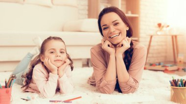 Anne ile kızı eğlenceli. Evde dinlenin. Çocuk gelişimi. Anne ve kızı kullan. Mutlu anne ve çocuk pijama. Anne ve kız halı üzerinde yalan. Renkli kalemler. Kadın ve kızı çizmek. Beyaz iç