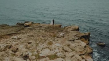 Kayalık bir tepede iki kişi. Kayalık bir deniz kıyısında bir çift aşık.