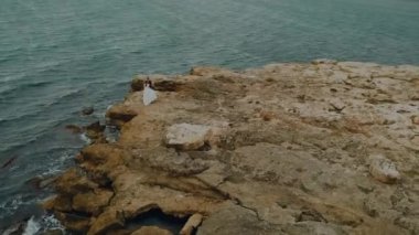 Kayalık bir tepede iki kişi. Kayalık bir deniz kıyısında bir çift aşık.