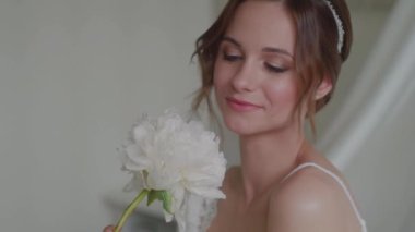 Güzel, gülümseyen bir kadın elinde kocaman bir çiçeğe bakar..