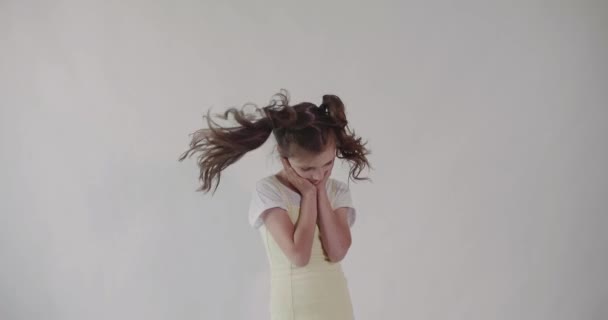 Een jong meisje met twee paardenstaarten draait haar hoofd en schudt met haar haar. geïsoleerd. — Stockvideo