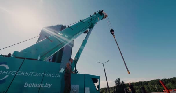 Bělorusko, Minsk - 30. července 2020: Stavitelé se připravují na zajištění nákladu na hácích pojízdného jeřábu. Světlice objektivu. — Stock video