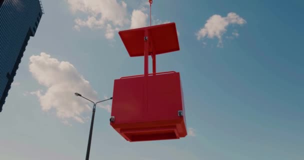 Primer plano de una cuna de edificio naranja levantada por una grúa se eleva hasta un rascacielos — Vídeos de Stock