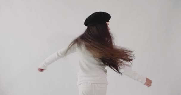 Biała dziewczyna w berecie z długimi ciemnymi włosami kręci się z otwartymi ramionami. Izolacja. — Wideo stockowe