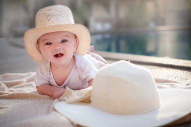 Şapkalı bir bebek havuzun kenarında dinleniyor. Güneşlenir.