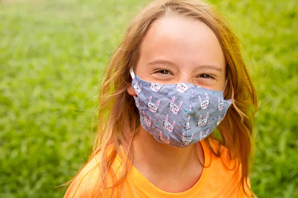 Çocuk maskeli mutlu bir kız gülümsüyor. Çocuk parkta yürüyor..
