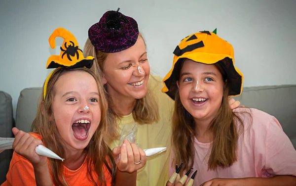 快乐的家庭正在为万圣节做准备 妈妈和女孩画彼此 戴帽子笑着的妇女和儿童 — 图库照片