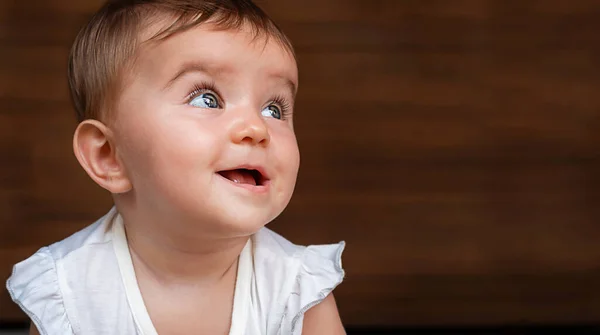 Tahta arka planda beyaz elbiseli gülümseyen bebeğin portresi..