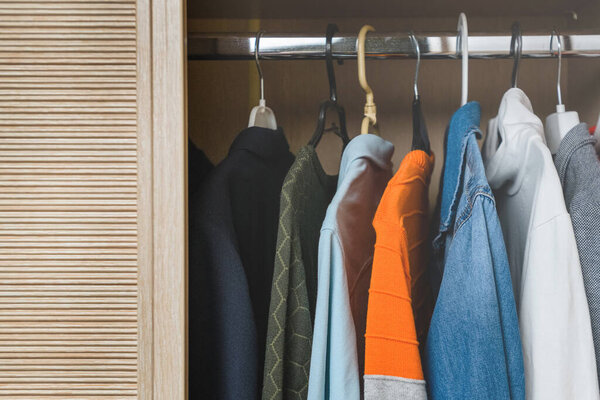 Разнообразная разноцветная одежда для подростка висит в шкафу на вешалках
.