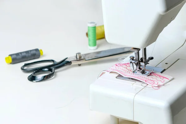 Sewing machine and sewing accessories: scissors, threads, ribbons on the table in the room. Concept - sewing as a hobby