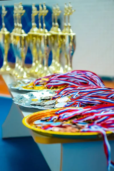 Medals and cups are on the table to award winners in children\'s artistic gymnastics competitions. Medals out of focus.