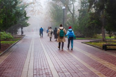 Sonbaharda şehirde sabah sisi. Sırt çantalı bir adam ve bir kadın sokakta yürüyorlar. Konsept - üniformalı unisex.