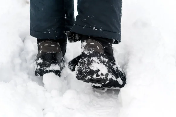 A boy walks in the snow, field, meadow. Winter black boots with a membrane, covered with snow. Close-up