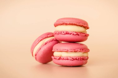 Bej arka planda beyaz çikolata kremalı üç pembe bademli kurabiye.