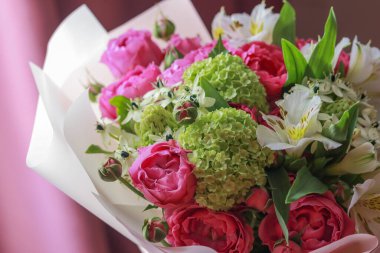 Pembe-yeşil gül buketi, beyaz zambaklar, mor arka planda ortancalar