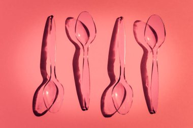 Pembe arka planda tek kullanımlık plastik kaşıklar ve zıt gölgeler.