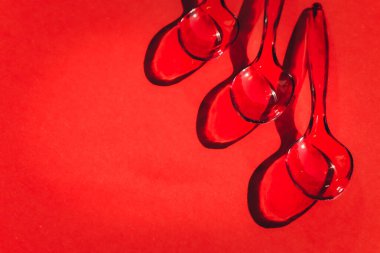 Kırmızı arkaplanda tek kullanımlık plastik kaşıklar ve zıt gölgeler.