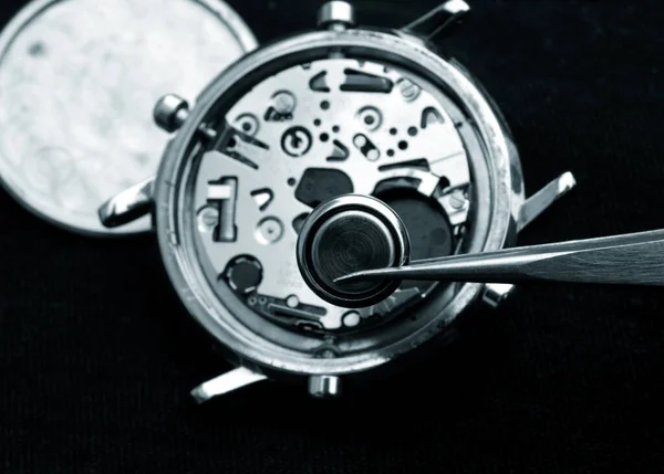 watchmaker changing battery, close up of watch battery and quartz watch caliber in the background