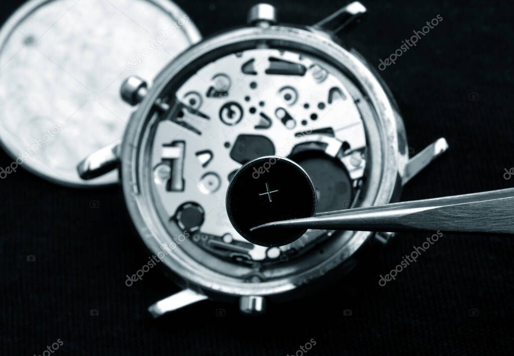 watchmaker change battery, close up of battery and quartz watch caliber in the background monochrome in blue image