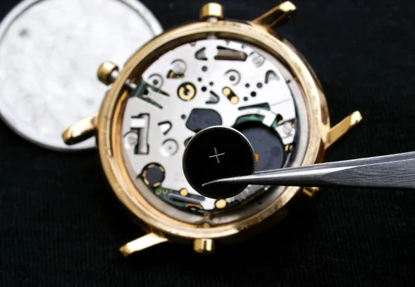 watchmaker change battery, close up of battery and quartz watch caliber in the background