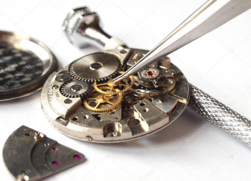 watchmaker working on vintage watch mechanism taking small gear with tweezers