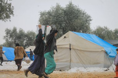 Halep, Suriye 15 Şubat 2017 Bir mülteci kadın kamptaki kar sırasında kafasında bir kova su tutuyor.