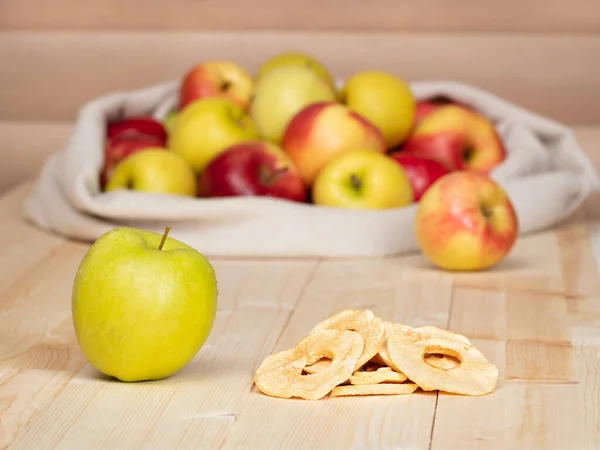 Tahtadaki elma çuvalının arka planında yeşil elma ve kurutulmuş elma dilimleri.
