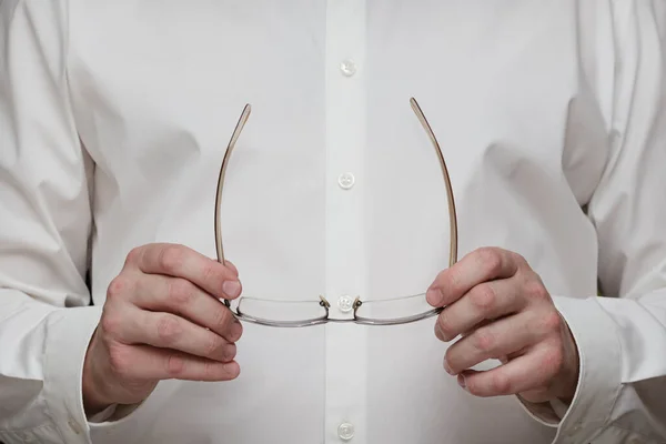 Man in a white business shirt hold the glasses in hands before itself, close up