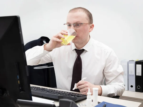 Sick man in a white business shirt and red tie working in office on a desktop computer, hold crumpled napkin and drinking a vitamin drink from glass, close up