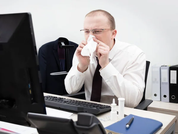 Man working in office on a computer in a white business shirt and red tie have got running nose and blows his nose to a napkin, close up