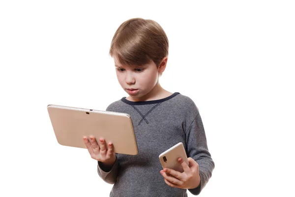 Yakışıklı bir Avrupalı çocuğun portresi akıllı telefon ve tablet bilgisayarı tut ve beyaz arkaplanda merak uyandıran bir şekilde tablete bak.