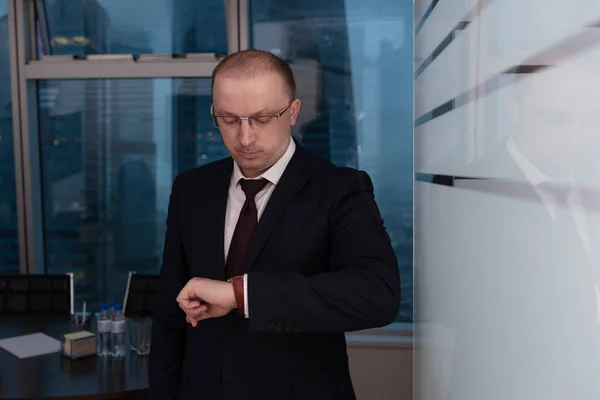 Toplantı odasının müdürü, toplantı saatini kontrol etmek ve katılımcıları beklemek için saate bakıyor, kapatın.