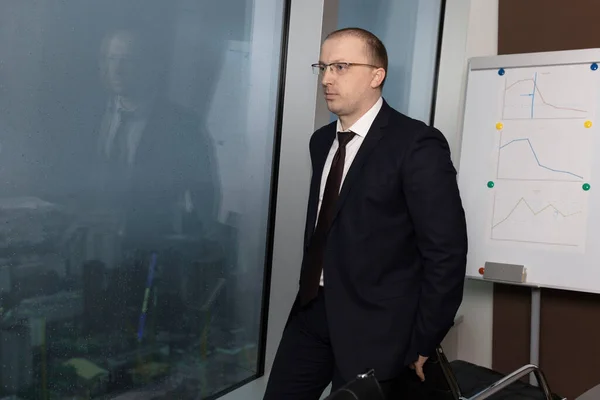 Mavi takım elbiseli yönetici koltuğun arkasında oturur ve düşünceli bir şekilde panoramik pencerenin dışındaki yağmura ve bulutlara bakar.
