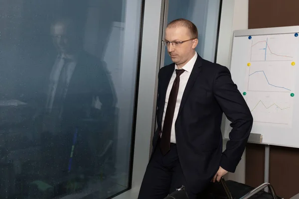 Resmi takım elbiseli düşünceli ve üzgün bir yönetici akşamleyin pencerenin yanında oturuyor ve önünde yağmur damlaları var. Kapatın.